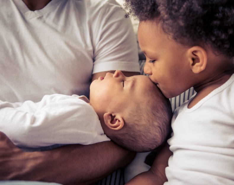 child kisses top of infants head